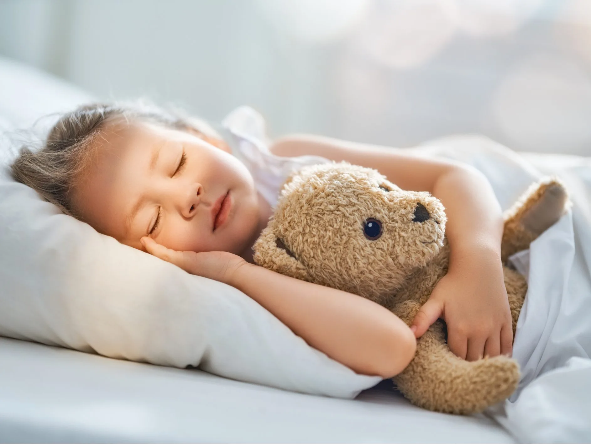child is sleeping in the bed Adorable little child is sleeping in the bed with her toy. The girl is hugging the teddy bear.