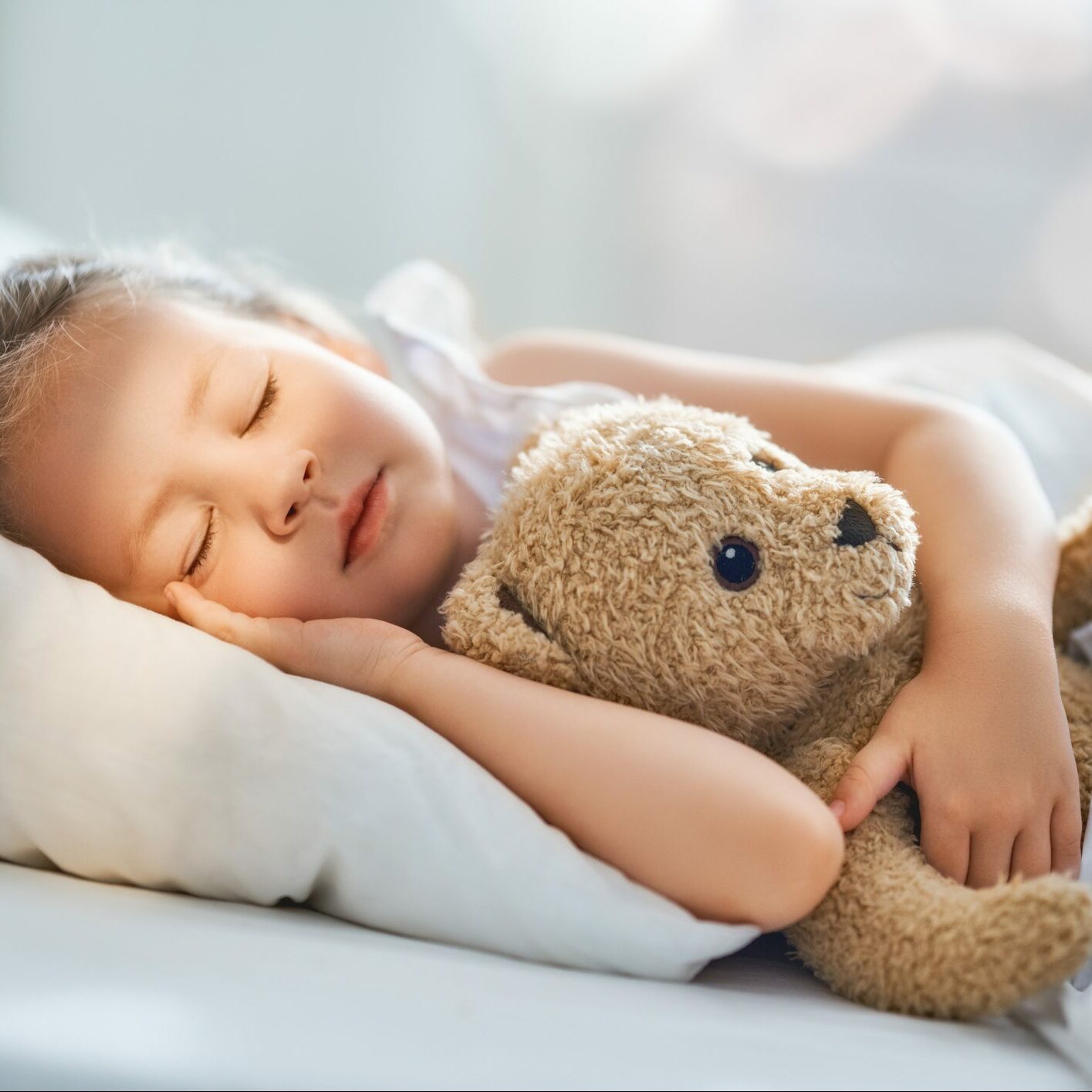 Bedårende lille barn sover i sengen med sit legetøj. Pigen krammer bamsen.